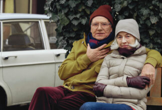 Ein älteres Paar sitzt auf einer Bank. Er hat seinen Arm um sie gelegt.