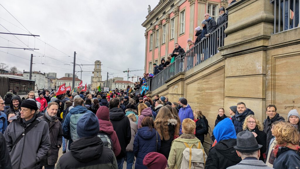 Viele Menschen stehen und gehen an der Fassade des Landtags in Potsdam entlang. Sie bilden eine Menschenkette.