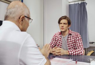 In einer Praxis sitzen sich ein Arzt und sein Patient gegenüber und sprechen miteinander.
